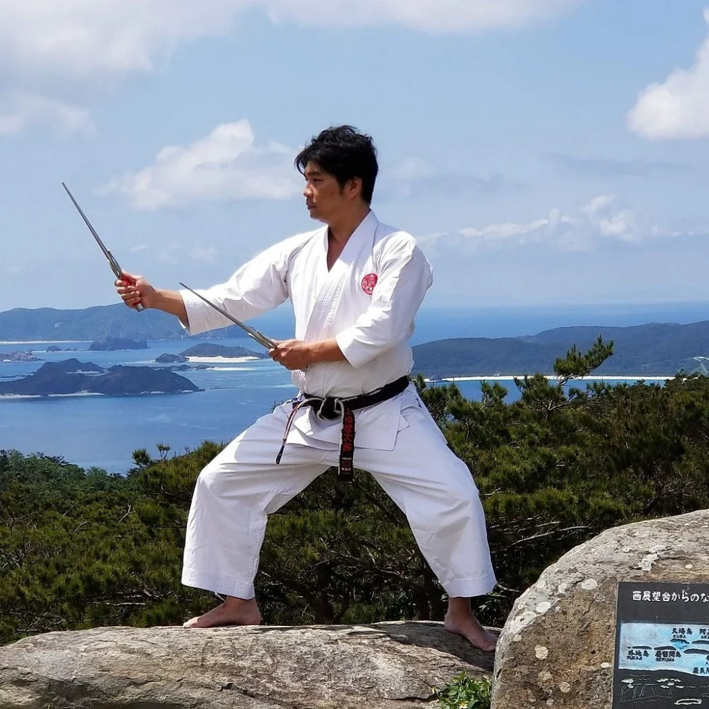 Karateka practicing sai at a scenic Okinawa overlook