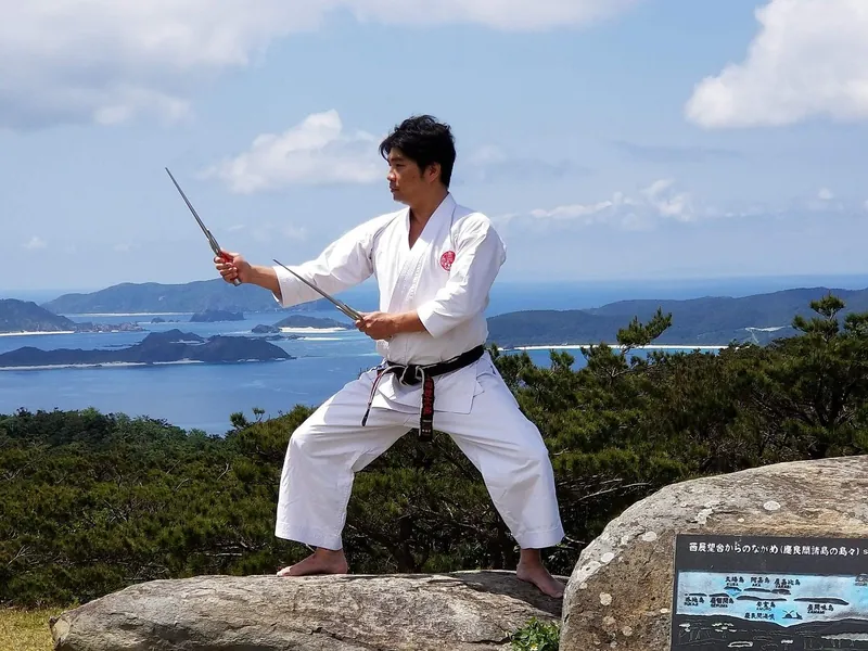 Okinawan karate master performing a sword kata on a rock overlooking the sea and islands