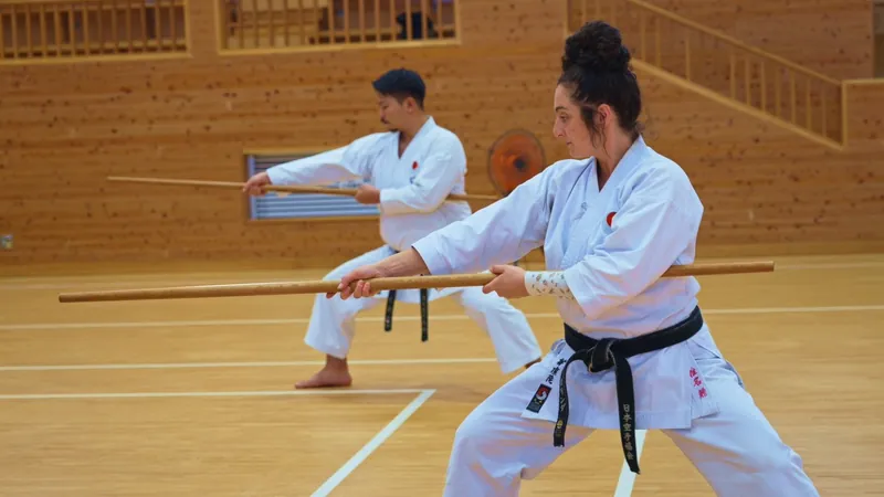 Two karateka training with bo staffs on a wooden dojo floor in Okinawa