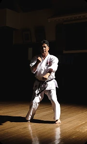 A karateka holding a low stance in a dimly lit dojo