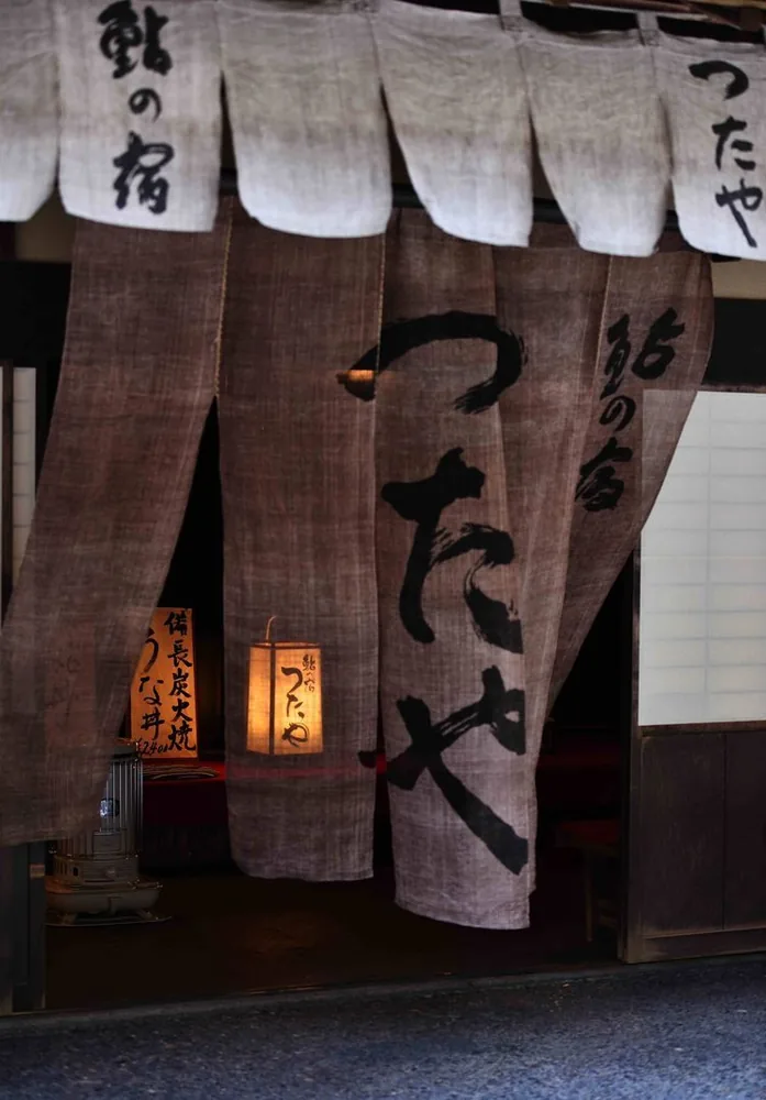 Traditional noren curtains and a lit paper lantern outside a Japanese eatery